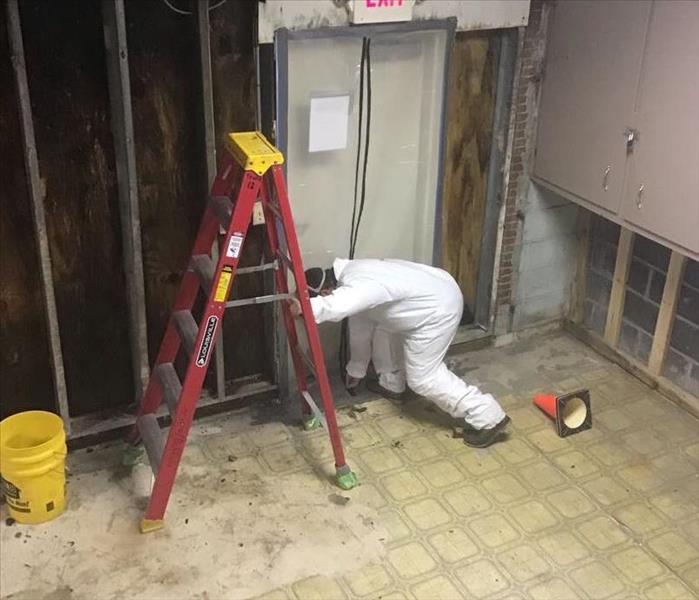 The photo shows a SERVPRO employee wearing a tyvek suit performing demo work.